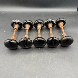 May include: Five antique black glass door knobs with aged metal stems. The knobs are round with a glossy finish, showing signs of wear. The stems are a rusty brown color, and the knobs are arranged in a row.