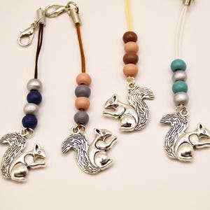 Puede incluir: Cuatro colgantes con abalorios de ardilla plateada. Cada abalorio tiene una combinación de colores diferente: azul oscuro y plata, marrón y gris, marrón y marrón claro, y turquesa y plata. Los abalorios están sujetos a un cierre.