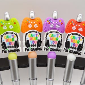 May include: A selection of stylus pens with gaming-themed designs. Each pen has a controller-shaped top in different colours, with the text "Can't Hear You I'm Gaming". The pens have silver barrels and coloured tips.