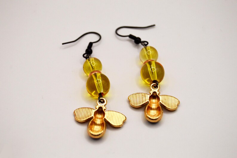 Pu&ograve; includere: Un paio di orecchini a forma di ape color oro con ganci neri. Ogni orecchino presenta tre perline gialle e un ciondolo a forma di ape dettagliato. Gli orecchini sono progettati per ciondolare.