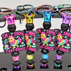May include: Four colorful keychains with a black background and a cartoon chicken with the text "I'm 100% That Chick" on each keychain.