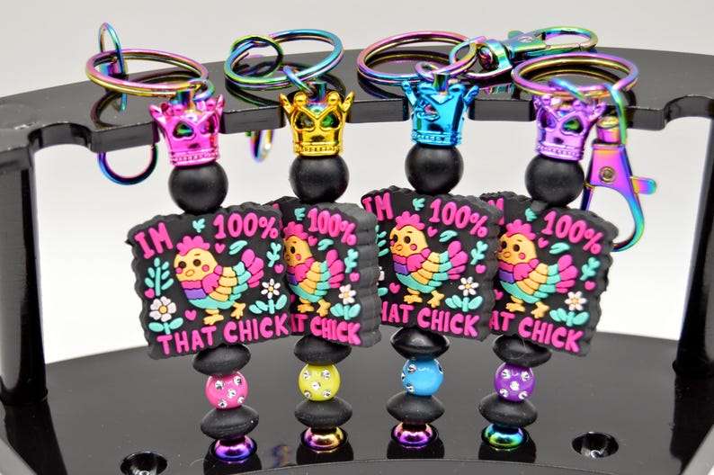 May include: Four colorful keychains with a black background and a cartoon chicken with the text "I'm 100% That Chick" on each keychain.