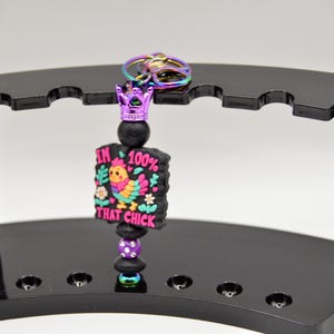 May include: A black and purple keychain with a crown charm and a colorful cartoon chicken with the text "I'm 100% That Chick".