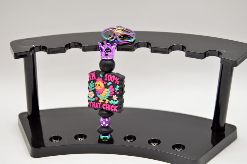 May include: A black and purple keychain with a crown charm and a colorful cartoon chicken with the text "I'm 100% That Chick".