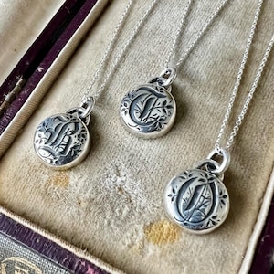 May include: Three silver necklaces with initial charms in a velvet-lined jewelry box. The charms are engraved with the letters "L", "T", and "O".