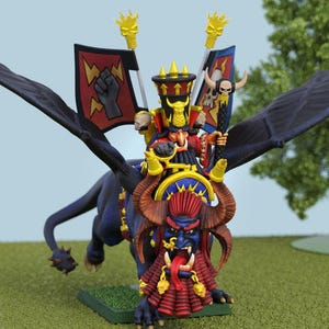 Könnte beinhalten: Miniatur-Fantasy-Figur einer geflügelten Kreatur mit einem Reiter. Die Kreatur ist dunkelblau mit großen Flügeln. Der Reiter trägt ein rot-goldenes Outfit und sitzt auf einem gehörnten, blaugesichtigen Dämon. Die Figur hat Banner mit Blitzen und einer Faust.