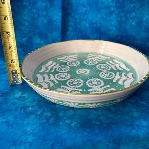Puede incluir: Un plato redondo de cer&aacute;mica con borde blanco e interior turquesa decorado con motivos florales blancos. El plato mide aproximadamente 6,3 cm de alto y 20 cm de di&aacute;metro. Una cinta m&eacute;trica amarilla est&aacute; al lado del plato.