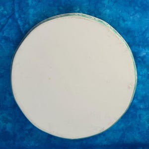 Puede incluir: Un plato redondo de cer&aacute;mica blanca con un borde decorativo verde y turquesa. El plato est&aacute; sobre un fondo azul.