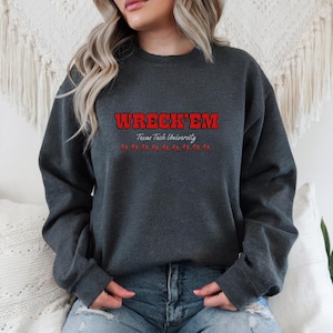 May include: Dark gray sweatshirt with the text "WRECK'EM" in red block letters above "Texas Tech University". Below the text are red stylized images. The sweatshirt is a crew neck style.