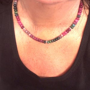 Peut inclure: Un collier de perles multicolores avec un d&eacute;grad&eacute; de perles roses, vertes et rouge fonc&eacute;. Le collier est orn&eacute; de petits espaceurs argent&eacute;s. Le collier est port&eacute; sur un haut noir.