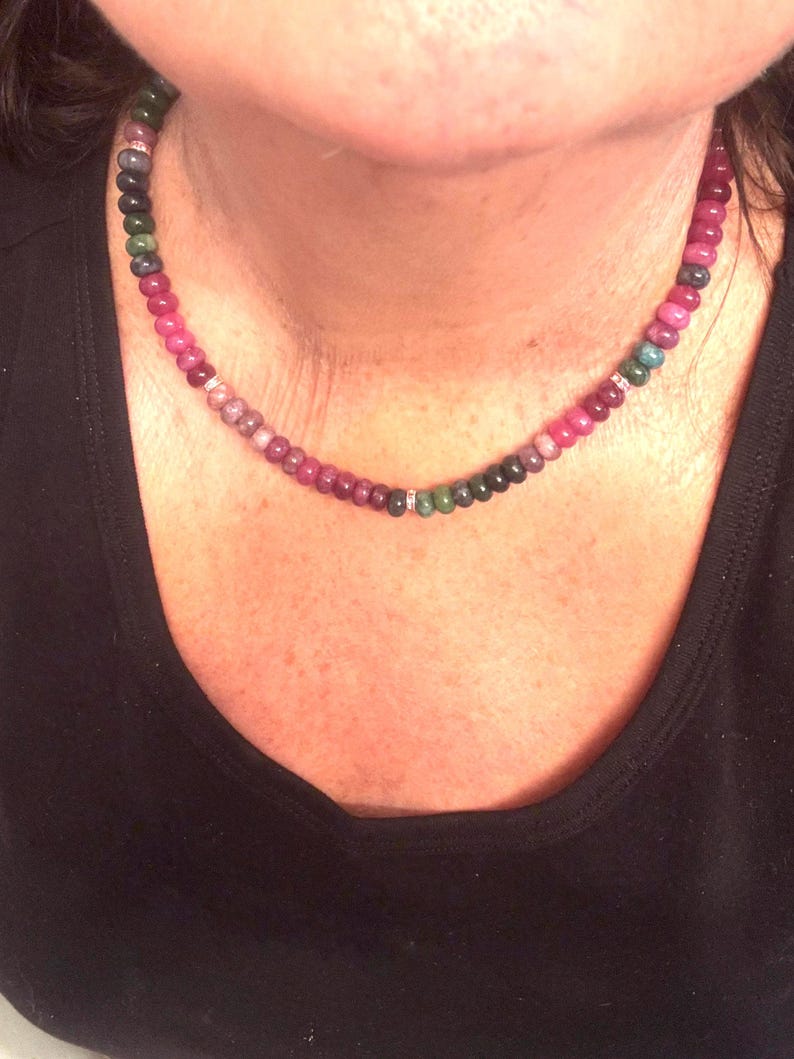 Peut inclure: Un collier de perles multicolores avec un d&eacute;grad&eacute; de perles roses, vertes et rouge fonc&eacute;. Le collier est orn&eacute; de petits espaceurs argent&eacute;s. Le collier est port&eacute; sur un haut noir.