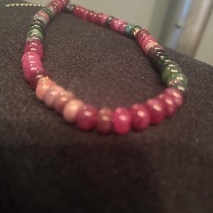 Peut inclure: Un collier de perles compos&eacute; de diverses pierres pr&eacute;cieuses color&eacute;es. Les perles passent du rouge profond au rose, vert et noir. Le collier est mont&eacute; sur une cha&icirc;ne d&eacute;licate, cr&eacute;ant un accessoire vibrant et accrocheur.