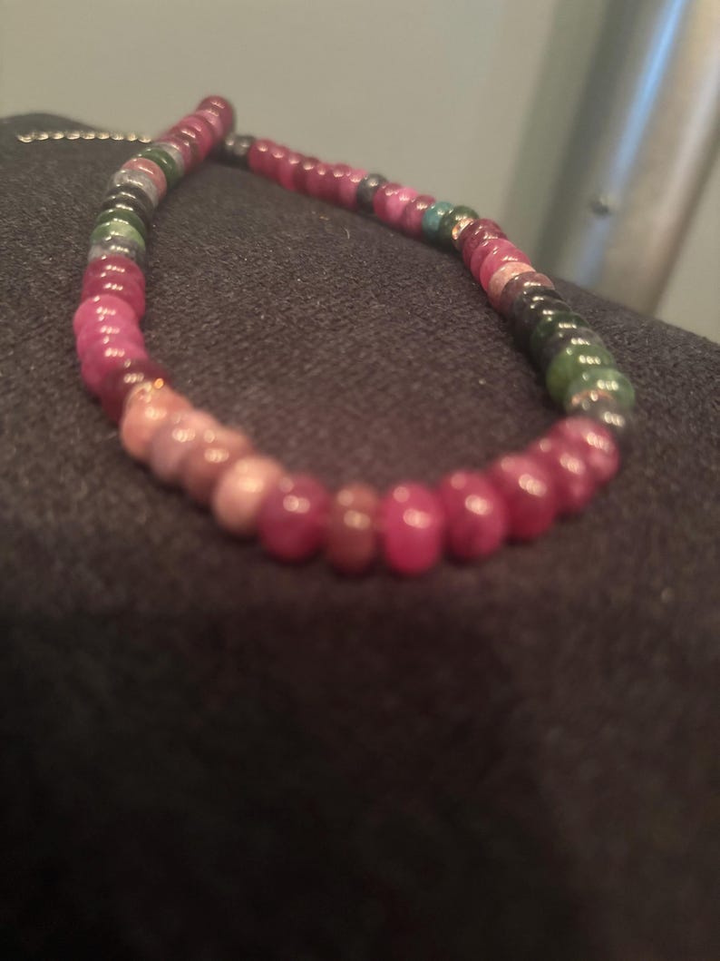 Peut inclure: Un collier de perles compos&eacute; de diverses pierres pr&eacute;cieuses color&eacute;es. Les perles passent du rouge profond au rose, vert et noir. Le collier est mont&eacute; sur une cha&icirc;ne d&eacute;licate, cr&eacute;ant un accessoire vibrant et accrocheur.
