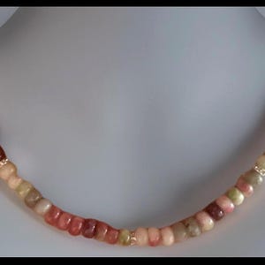 Puede incluir: Un collar con una cadena de cuentas redondeadas multicolores en tonos rojos, rosas, verdes y beiges. Las cuentas est&aacute;n ensartadas con detalles dorados. El collar se exhibe en un busto de maniqu&iacute; blanco.