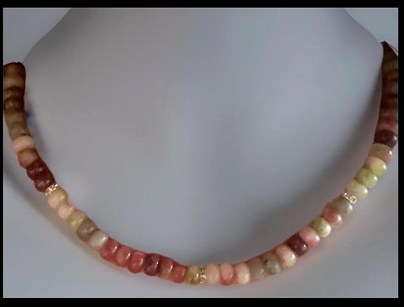 Puede incluir: Un collar con una cadena de cuentas redondeadas multicolores en tonos rojos, rosas, verdes y beiges. Las cuentas est&aacute;n ensartadas con detalles dorados. El collar se exhibe en un busto de maniqu&iacute; blanco.