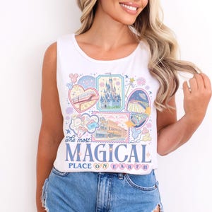 Pu&ograve; includere: Canotta bianca con una grafica colorata raffigurante varie attrazioni di parchi a tema e la scritta "The most MAGICAL PLACE ON EARTH". Il design include immagini di un castello, un treno e altri elementi stravaganti.