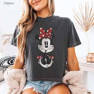 May include: Dark gray t-shirt featuring a distressed Minnie Mouse graphic with a red polka dot bow. The shirt has a crew neck and short sleeves. The word "Pepper" is in the top left corner.