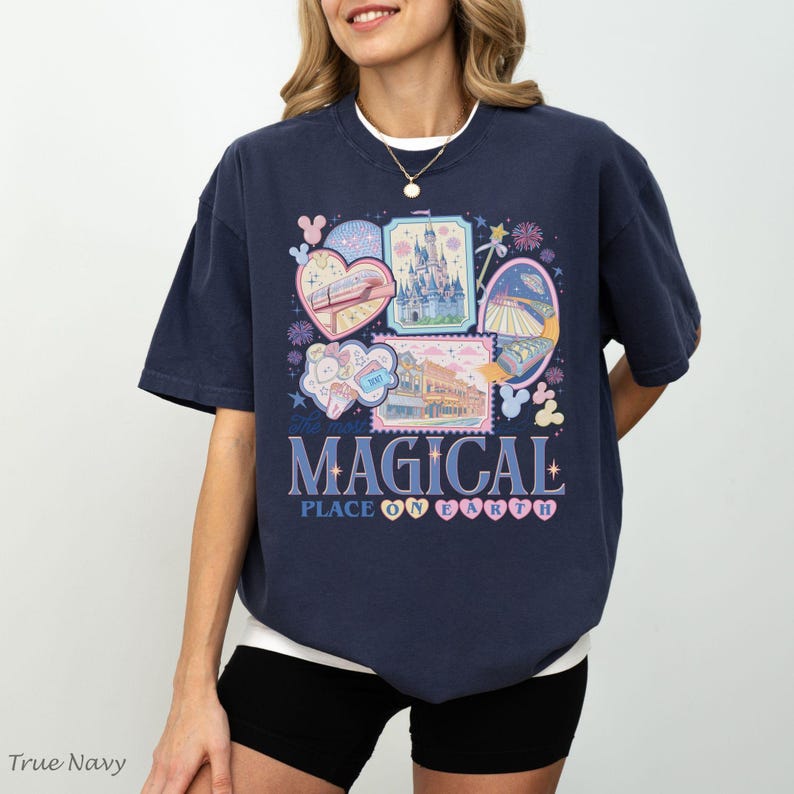 Pu&ograve; includere: T-shirt blu navy con un design grafico colorato con varie illustrazioni e la scritta "MAGICAL PLACE ON EARTH". Il design include immagini di un castello, un treno e altri elementi del parco a tema.