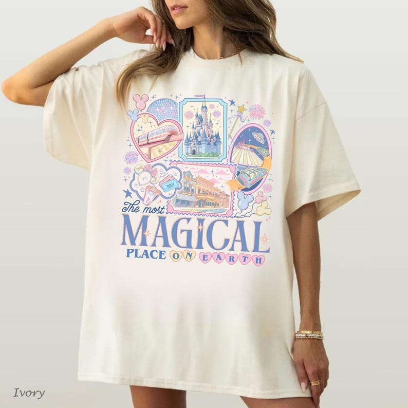 Pu&ograve; includere: T-shirt color avorio con grafica colorata con la scritta "The most MAGICAL PLACE ON EARTH". La grafica include immagini di un castello, un treno e altri elementi del parco a tema. La maglietta ha una vestibilit&agrave; ampia.