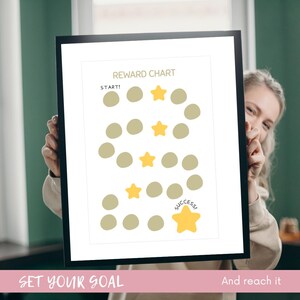 May include: A framed reward chart with a black border. The chart features a path of beige circles and yellow stars, with the words "Reward Chart" at the top and "Start!" and "Success!" at the beginning and end. The bottom reads "Set your goal and reach it."