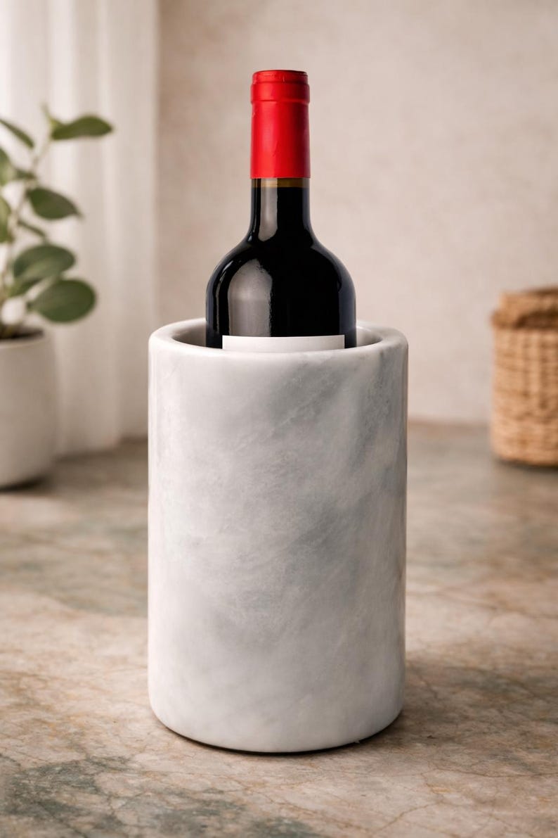 May include: A marble wine chiller holds a bottle of red wine. The wine bottle has a red cap and a white label. The chiller is cylindrical and has a gray and white marbled pattern.