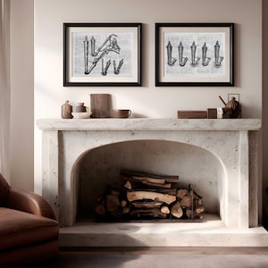Pode incluir: Duas impressões emolduradas em preto e branco de ilustrações vintage penduradas acima de uma lareira de pedra. A lareira exibe itens decorativos. Uma poltrona de couro fica à esquerda da lareira, e uma pilha de lenha está dentro.