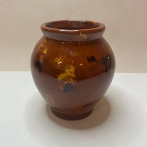May include: A small, round, brown ceramic vase with a wide opening. The vase has a glossy finish with patches of yellow and black. The vase is likely used for decorative purposes or to hold small items.