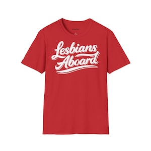 Könnte beinhalten: Rotes T-Shirt mit dem weißen Schriftzug "Lesbians Aboard" in kursiver Schrift. Der Text hat einen Schatteneffekt, der ihm ein dreidimensionales Aussehen verleiht. Das T-Shirt ist einfarbig.