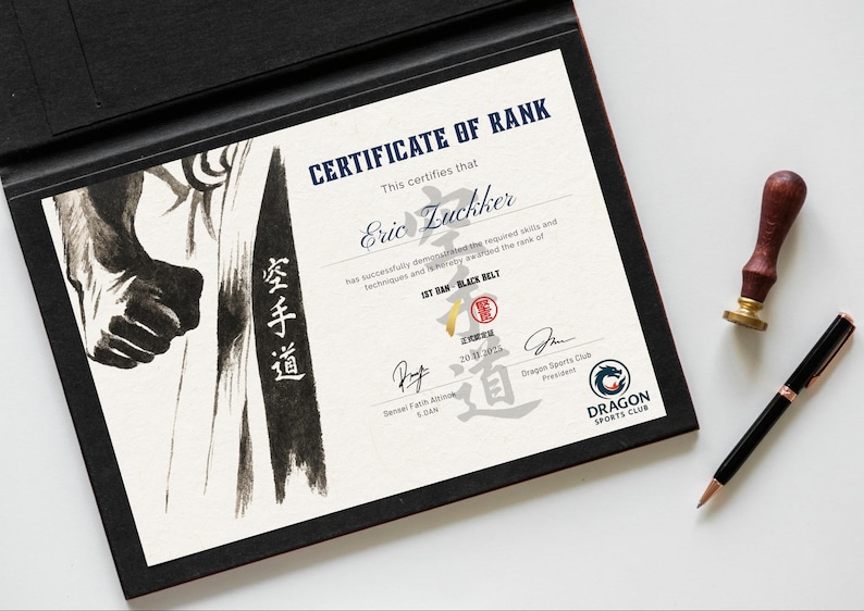 May include: A framed certificate of rank for Eric Luckker, 1st Dan Black Belt. The certificate features the text "Certificate of Rank" and the "Dragon Sports Club" logo. A pen and a stamp are placed beside the certificate.