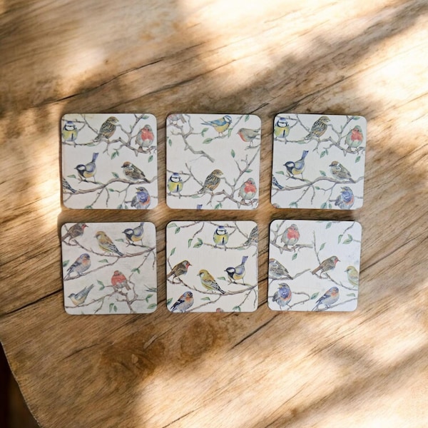 Peut inclure: Six dessous de verre carrés avec un motif d'oiseaux et de branches. Chaque dessous de verre présente un arrangement différent d'oiseaux colorés perchés sur des branches d'arbres sur un fond crème. Les dessous de verre sont disposés sur une surface en bois.