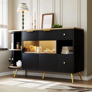 Puede incluir: Un aparador negro y con detalles en madera con detalles dorados. El mueble cuenta con múltiples compartimentos de almacenamiento, incluyendo cajones y una zona de exhibición con puertas de cristal. Las manijas y patas doradas añaden un toque de elegancia. Una lámpara, velas y arte enmarcado están encima.