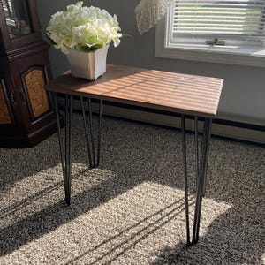May include: A rectangular wooden console table with a dark brown top and black hairpin legs. A white square vase with white flowers sits on the table. The table is approximately 30 inches long.