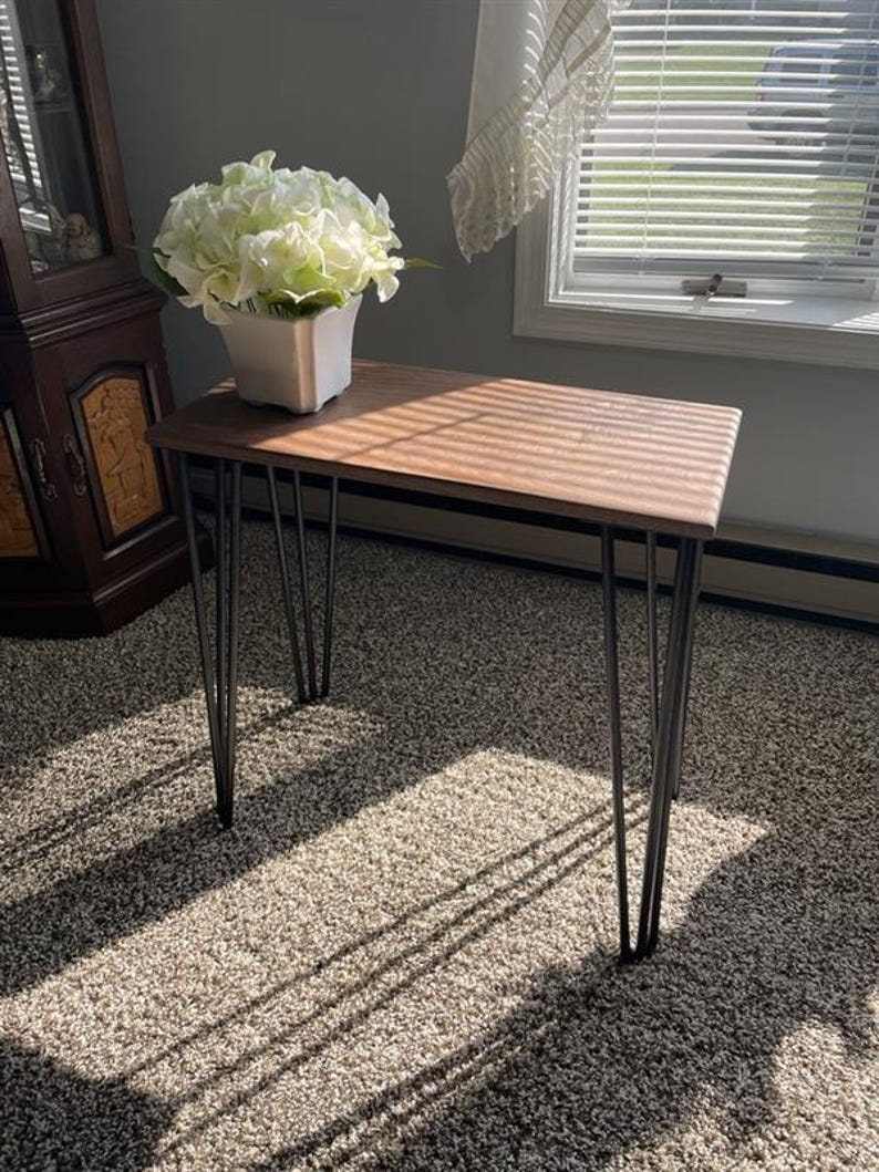 May include: A rectangular wooden console table with a dark brown top and black hairpin legs. A white square vase with white flowers sits on the table. The table is approximately 30 inches long.