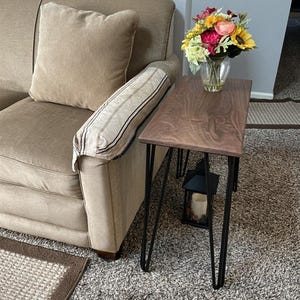 May include: A small, rectangular side table with a dark wood top and black hairpin legs. A vase of colorful flowers sits on the table. The table is next to a beige sofa.