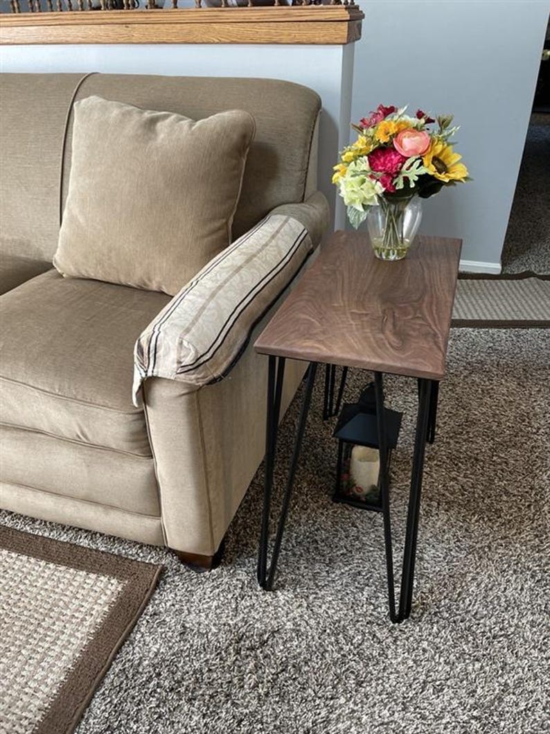 May include: A small, rectangular side table with a dark wood top and black hairpin legs. A vase of colorful flowers sits on the table. The table is next to a beige sofa.