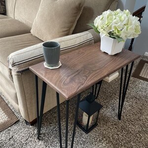 May include: A small, rectangular wooden side table with a dark walnut finish and black hairpin legs. A gray mug sits on a coaster, and a white square vase with green and white flowers is on the table. A black lantern is below.