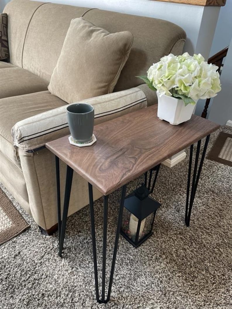 May include: A small, rectangular wooden side table with a dark walnut finish and black hairpin legs. A gray mug sits on a coaster, and a white square vase with green and white flowers is on the table. A black lantern is below.