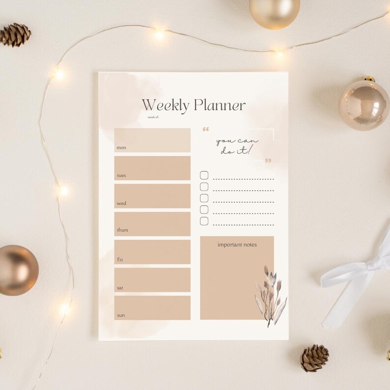 Op de afbeelding: Een weekplanner met een beige en wit aquarelontwerp. De planner bevat secties voor elke dag van de week, een notitiegedeelte en de tekst "you can do it!". Decoratieve elementen zijn bloemenillustraties en gouden ornamenten.