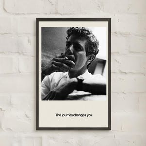 May include: Black and white framed print featuring a portrait of a person smoking a cigarette. The person is wearing a white shirt and has curly hair. The text "The journey changes you." is printed at the bottom of the print.