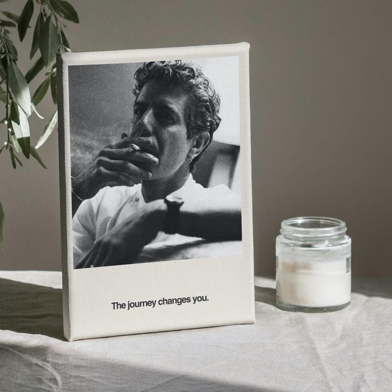May include: Black and white canvas print featuring a portrait of a man smoking, with the text "The journey changes you." A small glass jar with a white substance sits to the right of the print. The print is on a neutral-colored surface.