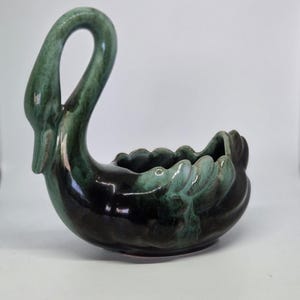 May include: A ceramic swan-shaped planter or bowl featuring a glossy finish with a blend of deep black and variegated forest green glaze. The swan has a long, curved neck and a scalloped edge along the body, creating a hollow centre for holding items.