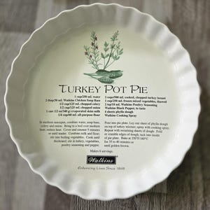 May include: A round, white ceramic pie dish with a fluted edge. The centre features a green herb illustration, the title Turkey Pot Pie, a list of ingredients with measurements in cups and mL, cooking instructions, and the Watkins brand logo.