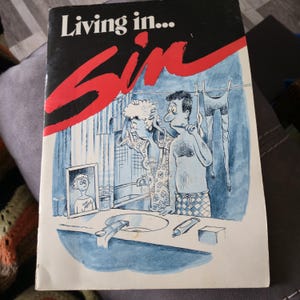May include: A book cover with the title "Living in... Sin" in white and red lettering. The illustration depicts a couple in a bathroom, with the woman applying makeup and the man brushing his teeth. A mirror shows a young boy.