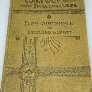 Peut inclure: Livre ancien intitulé "Elem. Arithmetic" de Kirkland & Scott, faisant partie de la "Gage & Co's Educational Series". La couverture est jaune-or délavé avec du texte noir et des éléments décoratifs, dont une illustration de lampe.