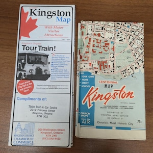 May include: Two vintage Kingston, Ontario maps. One is a brochure with a red maple leaf and the text "Greater Kingston Map" and "Tour Train!" The other is a Centennial Map of Kingston, with a detailed street layout.