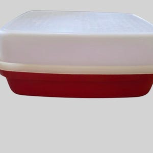 May include: A rectangular storage container featuring a deep red base and a contrasting off-white rim. The container is topped with a solid, opaque white lid that fits securely over the base, creating a clean and functional two-tone design.