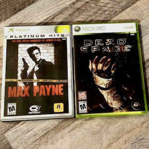 Op de afbeelding: Twee Xbox-gamecases. De eerste is "Max Payne" met een man die een pistool vasthoudt, de tekst "Platinum Hits" en een Mature-classificatie. De tweede is "Dead Space" met een robotische hand en een Mature-classificatie.