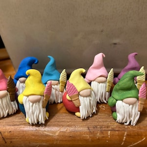 May include: A collection of eight miniature gnomes made of polymer clay, each holding a small ice cream cone. The gnomes are painted in various colors, including pink, yellow, blue, green, and purple.