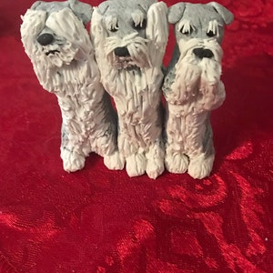 May include: Three small, gray and white, ceramic figurines of dogs. The dogs are standing in a row and have their paws covering their eyes. The dogs are on a red background.