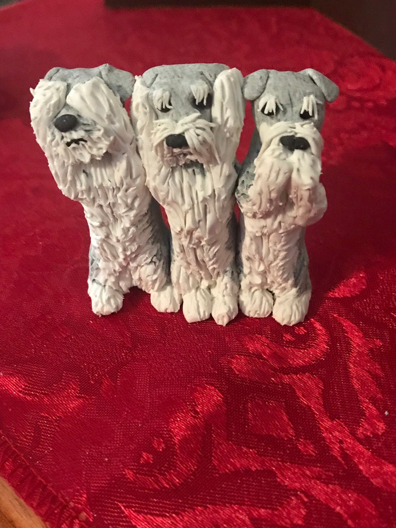 May include: Three small, gray and white, ceramic figurines of dogs. The dogs are standing in a row and have their paws covering their eyes. The dogs are on a red background.